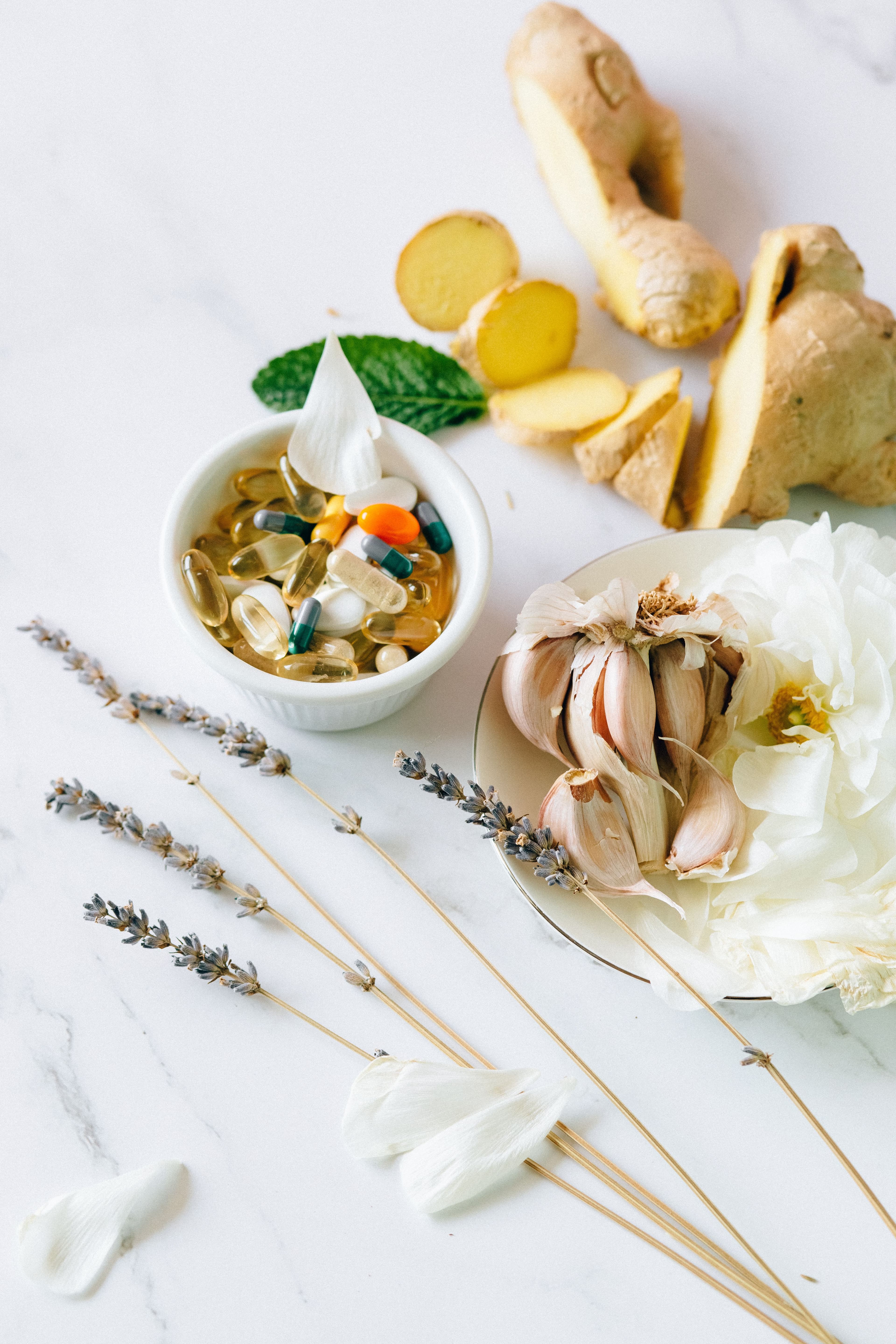 Ginger, garlic and lavender beside a bowl of herbal remedies on a marble surface