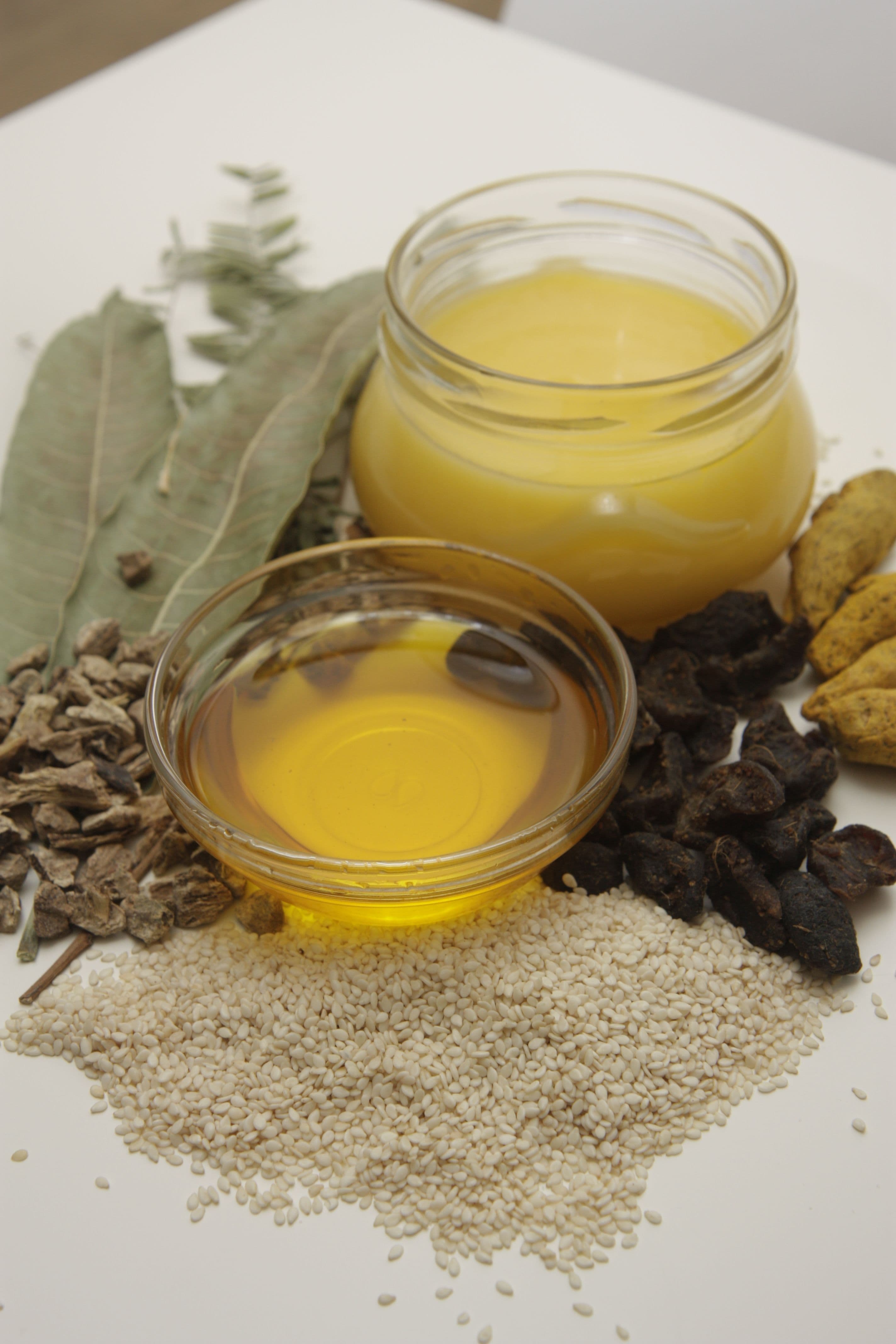 Ghee, oil and sesame seeds beside dried herbs and roots