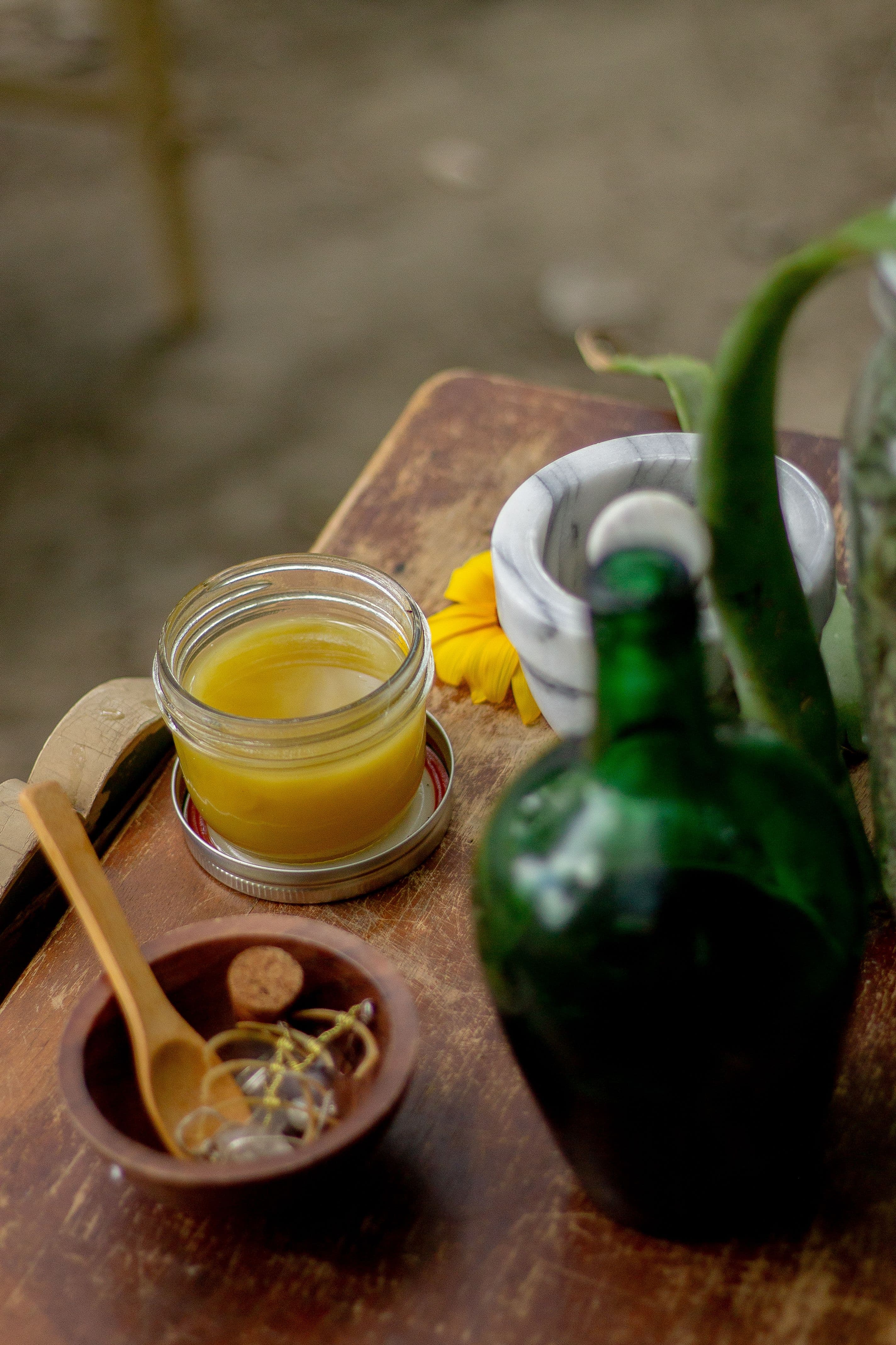 A jar of herbal balm beside a stone mortar and pestle, corked bottles alongside