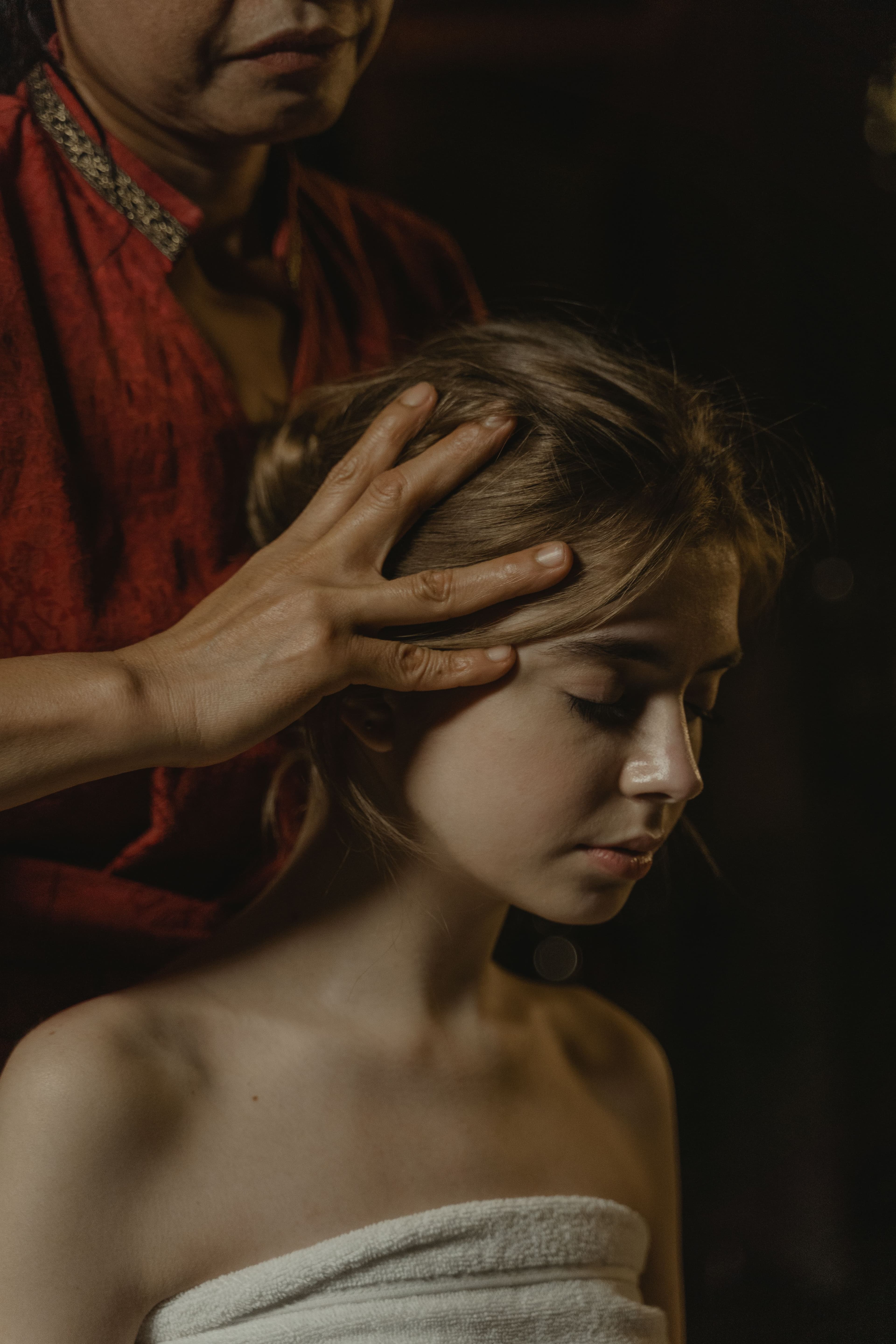 A therapist massaging a guest's scalp and temples in low, warm light