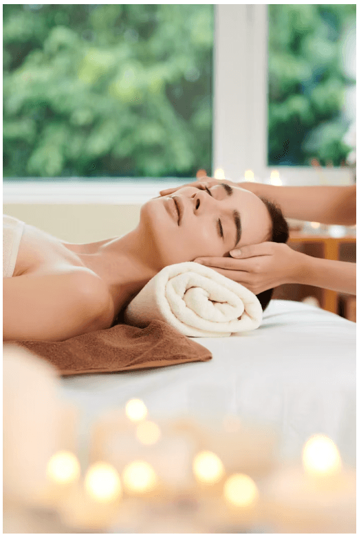 A therapist working along a guest's temples and jaw, candles glowing in the foreground